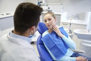 people, medicine, stomatology and health care concept - woman patient talking to male dentist and complain of toothache at dental clinic office